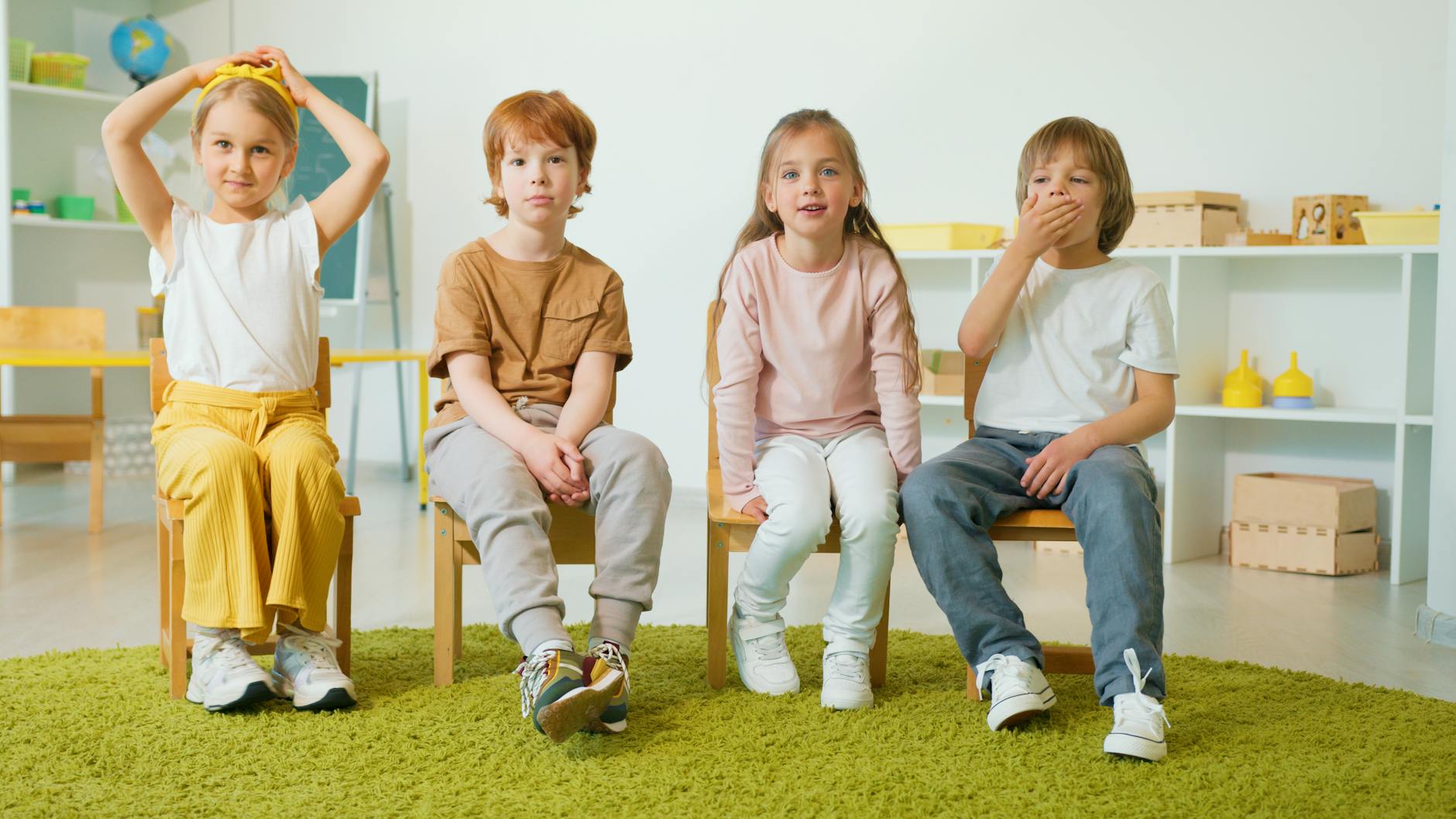 Group of children sitting on chairs in a classroom, smiling and engaged.
